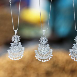 Close-up of beautiful silver necklaces with intricate designs hanging with a blurred background.
